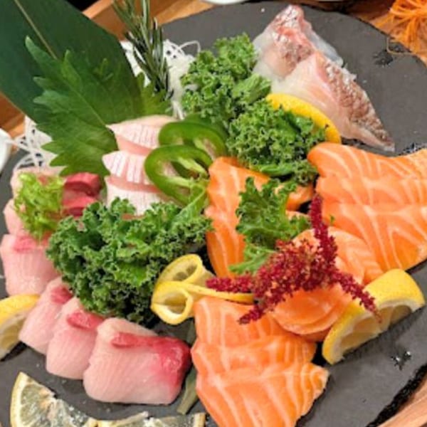 Assorted sashimi platter with salmon, tuna, and white fish, garnished with greens, lemon, and jalapeños.