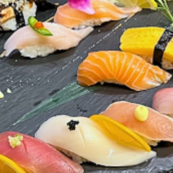 Assortment of colorful sushi and sashimi, including salmon, tuna, and yellowtail, on a dark plate.