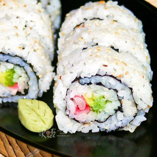 Two sushi rolls with white rice, sesame seeds, avocado, and pink ginger, served with wasabi.