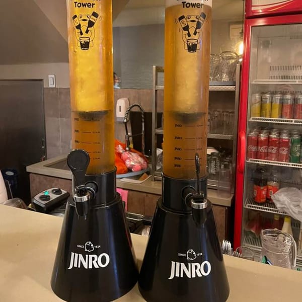 Two Jinro beer towers filled with golden liquid stand on a counter in a restaurant.