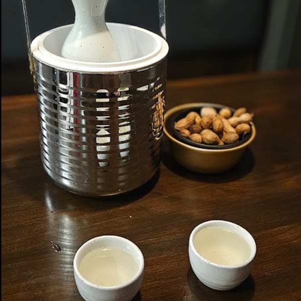 Sake carafe in a cooler with two cups of sake and a bowl of peanuts on a wooden table.