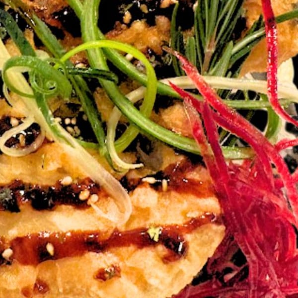 Close-up of crispy fried sushi with dark sauce, sesame seeds, green onions, and red garnish.