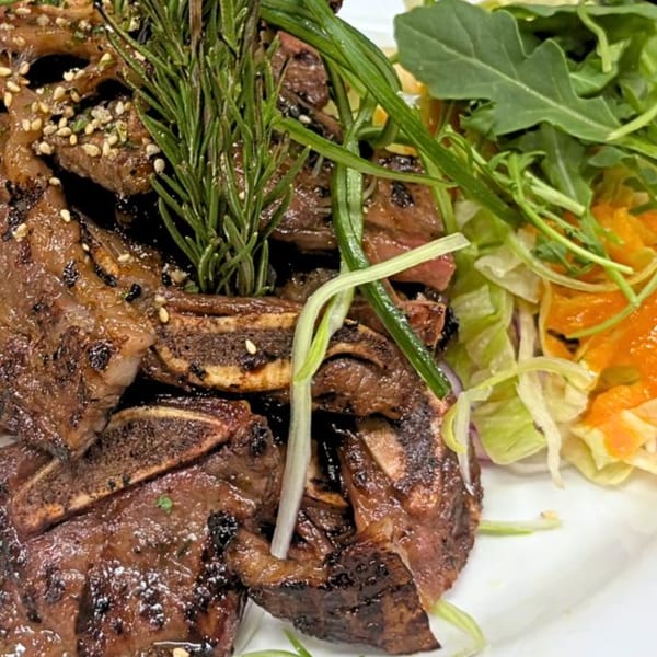 Grilled short ribs with sesame seeds and rosemary, served with a side salad.