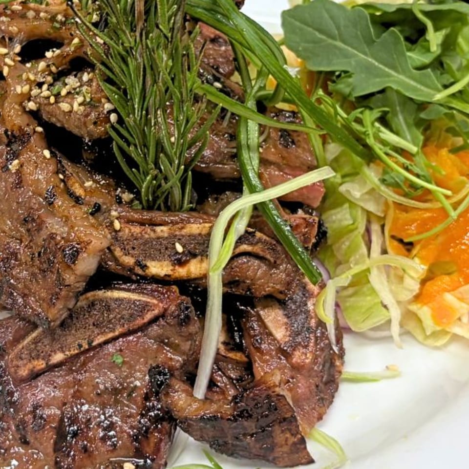 Grilled short ribs with sesame seeds and rosemary, served with a side salad.