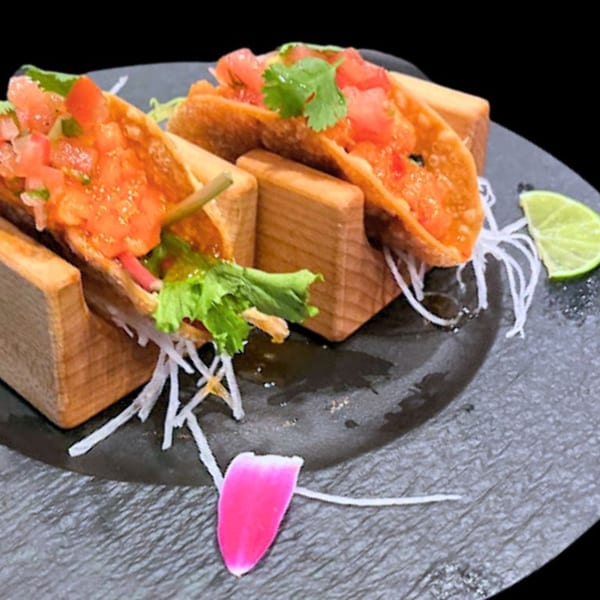 Two crispy sushi tacos with diced salmon, tomato, and cilantro, served on a dark plate.