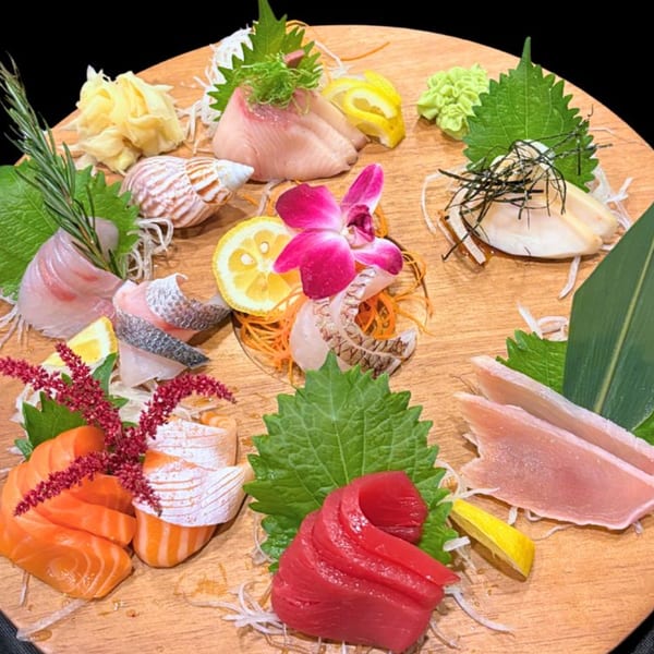 A large wooden platter with various sashimi, including salmon, tuna, and white fish, garnished with lemon and flowers.